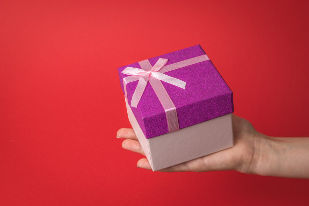 一个大礼品盒，在孩子的手在一个红色的背景。图片下载