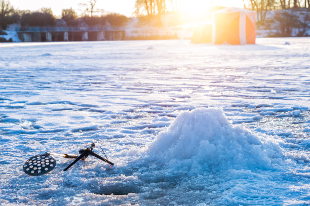 冬季鱼竿与一个弯曲点头在一个钻孔的背景上的大坝和钓鱼帐篷。图片下载