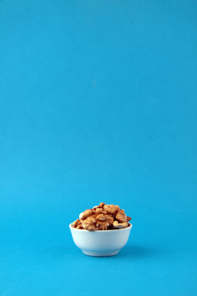 一碗去皮的核桃孤立在蓝色背景垂直图像图片下载