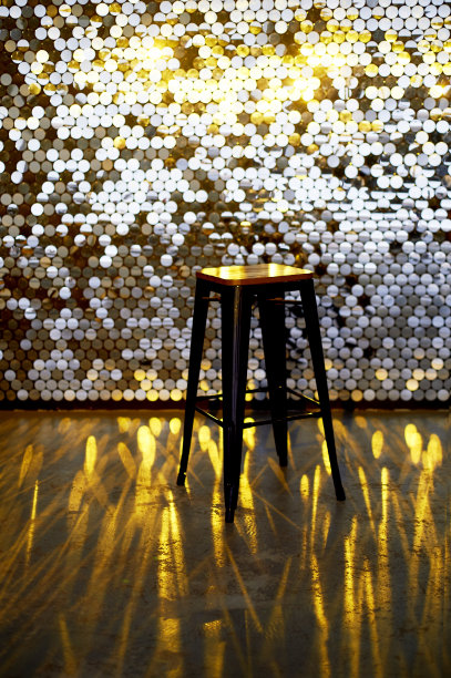 金属底座上的高凳子，映衬着带有亮片的墙壁背景。眩光反射在地板上。迷人的设计图片下载