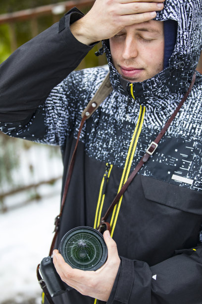 沮丧的年轻成年摄影师拿着相机与破碎的玻璃在镜头上图片下载