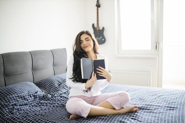 美丽的女人坐在她的床上，在早上看一本书图片下载