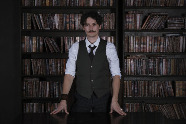 一个沉思的人晚上站在黑暗的图书馆房间里。留着小胡子的时尚男士拉直了手镯图片下载
