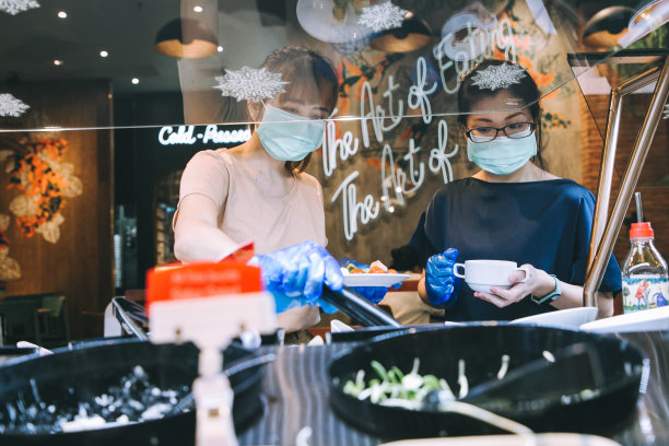 两名亚洲妇女戴着防护口罩和手套在餐厅挑选食物-库存照片图片下载