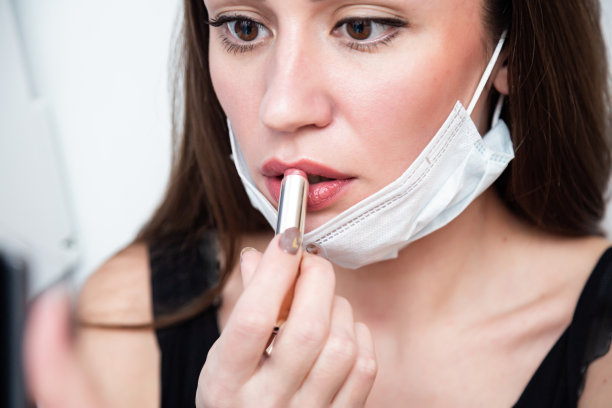 一个美丽的三十年的女人。女孩戴着防护面具，涂上口红，用智能手机代替镜子素材图片