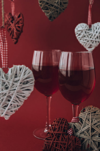 两杯红酒和心形装饰。爱浪漫。夫妇关系。红色哑光背景。白色和红色元素。情人节浪漫晚餐图片下载