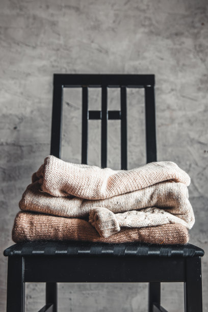 灰色墙边的椅子上放着一堆温暖舒适的针织毛衣。秋、冬的概念。图片下载