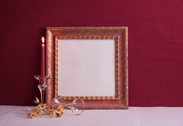 干枯的水仙花，一个长茎的烛台和一支燃烧着的蜡烛，桌子上有一个红色背景的旧相框图片下载