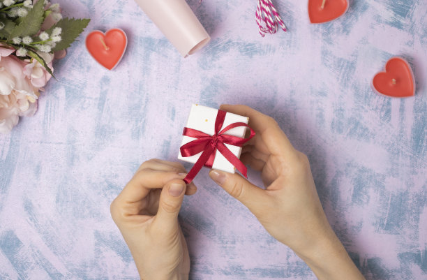 在灯光背景下，女性的手拉着礼品盒上的红丝带。致以圣诞和新年的问候。有选择性的重点图片下载