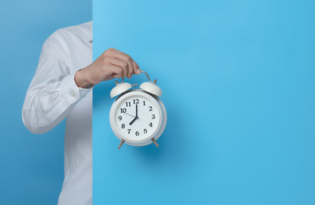 男子手持白色闹钟在蓝色背景，复制空间的文本图片下载