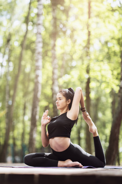 年轻女子穿着运动服在公园户外练习瑜伽，做着鸽子姿势。类篇rajakapotasana。图片下载