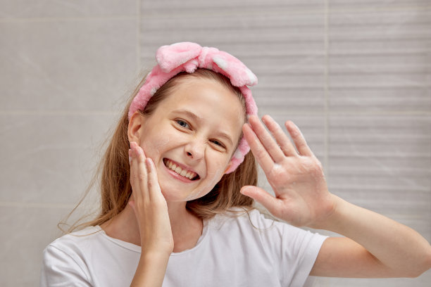 美丽的金发女孩在明亮的浴室里洗脸。图片下载