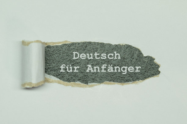 德语文本Deutsch für Anfänger -德语初学者出现在撕破的白纸后面。俯视图打开白纸和信息写在后面的灰色石头背景图片下载