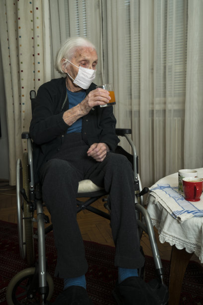 戴着面具坐在轮椅上的老妇人正在喝果汁图片下载