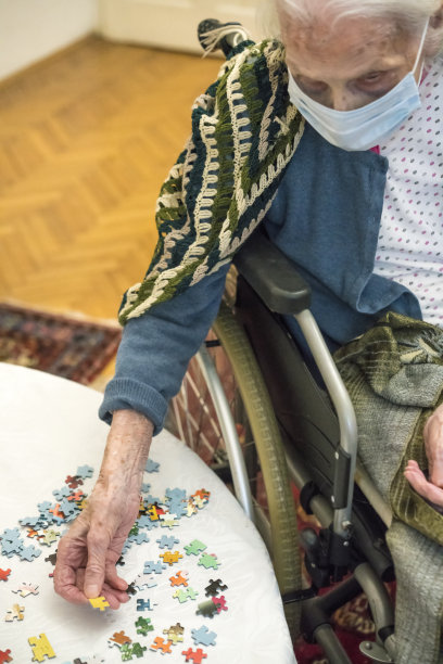 坐在轮椅上的老年妇女正在把一块拼图放在白色的桌子上，作为老年人的大脑训练图片下载
