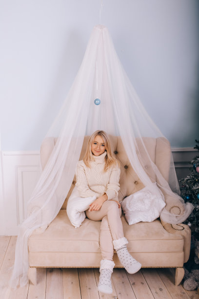 一个穿着白毛衣的金发美女坐在沙发上图片下载