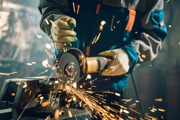 在特殊的衣服和护目镜的锁匠工作在生产。金属加工用角磨床。火花在金属加工图片下载