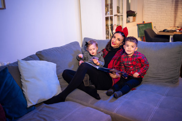 妈妈在圣诞树旁给女儿们读书。库存图片图片下载