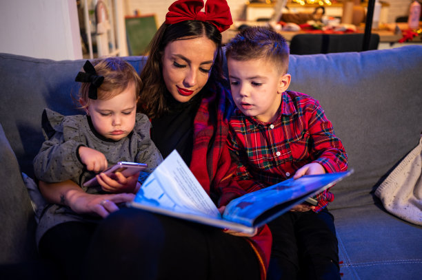 妈妈在圣诞树旁给女儿们读书。库存图片图片下载
