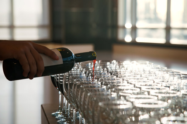 一名侍者将红葡萄酒从酒瓶倒到酒杯中，这是晚上为晚宴准备的。照片有一些眩光效应，从窗户后面的太阳背光。图片下载