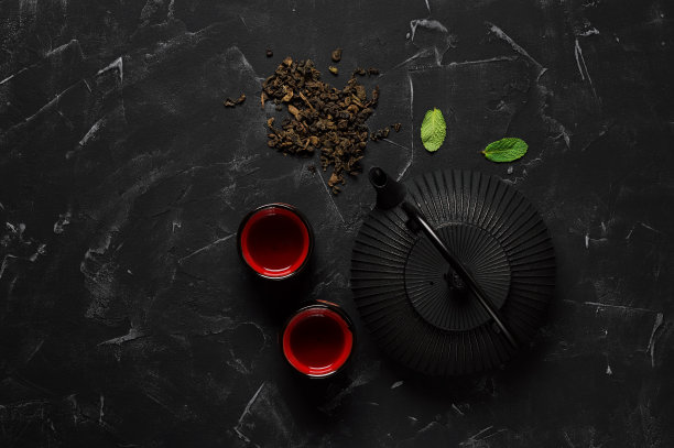 传统的亚洲茶道。黑色金属茶壶，茶杯，干茶在黑色的石头背景。俯视图，平放。图片下载