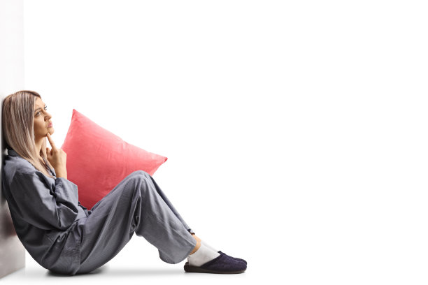 穿着睡衣的年轻女子坐在地板上，靠在墙上思考图片下载