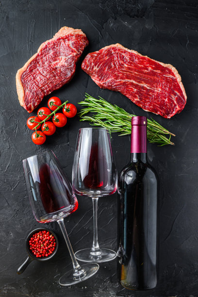Picanha生牛排与调味料和香草附近的一瓶和一杯红酒，在黑色纹理的背景俯视图图片下载