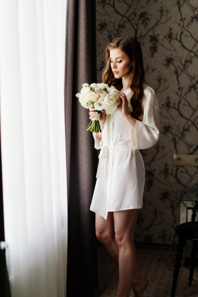 美丽的女人穿着白色长袍，窗前捧着婚礼花束图片下载