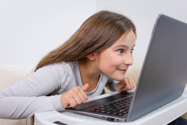 迷人的可爱的快乐微笑的女孩的肖像6-7岁的坐在使用笔记本电脑室内白色的背景远程学习图片下载