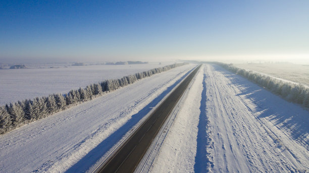 一架无人机从城市间田野的冬季道路上鸟瞰。无人机拍摄的冬季道路图片下载