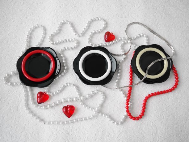 平的。一个美丽的组合，玻璃黑色的盘子，塑料首饰，手镯，珠子，红色的心在白色的背景。2月14日情人节的女性装饰品。仍然生活。图片下载