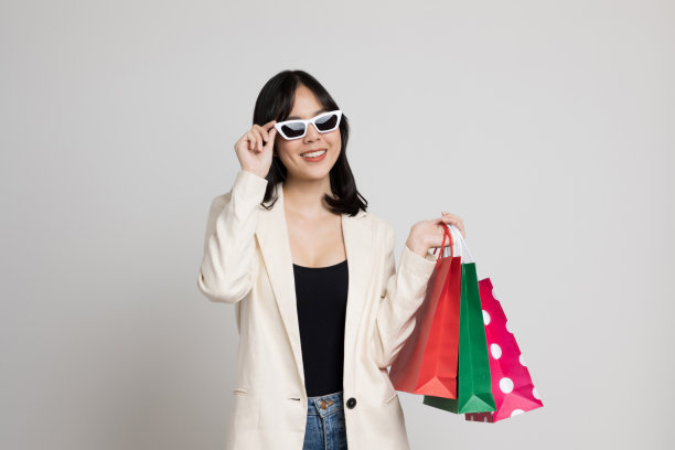 性感美丽的亚洲女孩手持购物袋孤立的白色背景。她戴着时髦的太阳镜。图片下载