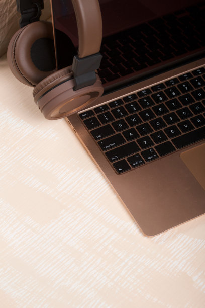 打开的粉色笔记本的碎片。附近是棕色的无线耳机。表面漆成白色和米色。图片下载