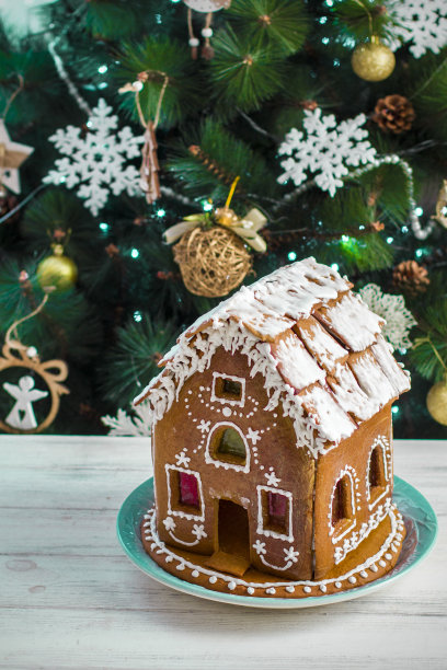 圣诞姜饼屋与釉在木头桌子上的背景圣诞树与燃烧的花环近距离。节日的气氛中。圣诞节的早晨。姜饼屋图片下载