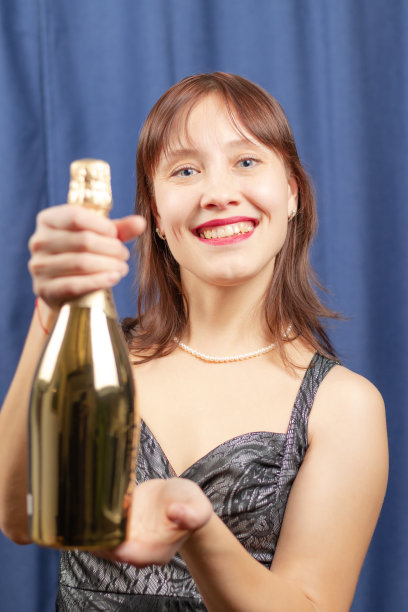 可爱的棕发女孩手里拿着一瓶金色的香槟，面带微笑。肖像图片下载