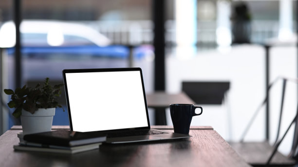 在木桌上模拟出空白屏幕、咖啡杯、盆栽和笔记本的平板电脑。空白屏幕用于图形显示蒙太奇。图片下载
