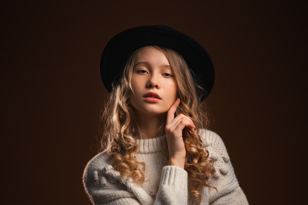 迷人的金发少女在黑帽子在工作室摆姿势在棕色的背景图片下载