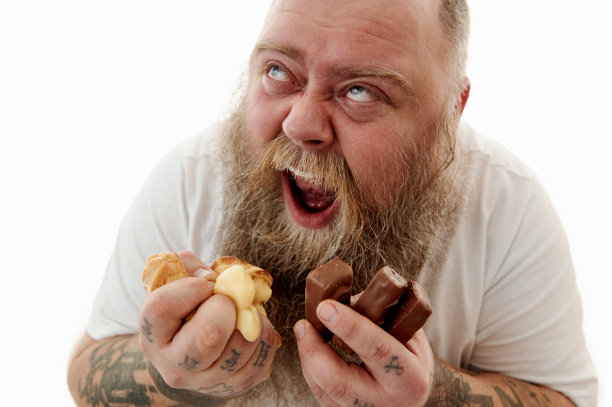 一个超重的男人用拳头挤巧克力棒来表达他的愤怒，痛苦和绝望，不恰当的生活方式导致了代谢综合症。孤立在白色背景上图片下载