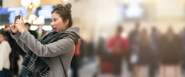 年轻的亚洲女性旅行者观光和享受冒险的时刻手用智能手机拍照以中央车站为背景，模糊人群背景图片下载
