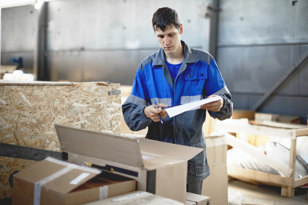 货物入库验收。一个穿着工装裤的年轻工人根据库存检查货物。图片下载