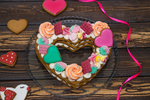 生日和情人节的节日甜点。心形蛋糕以蛋白酥、姜饼和奶油装饰，棕色的木质背景上点缀着红色的心形和丝带图片下载