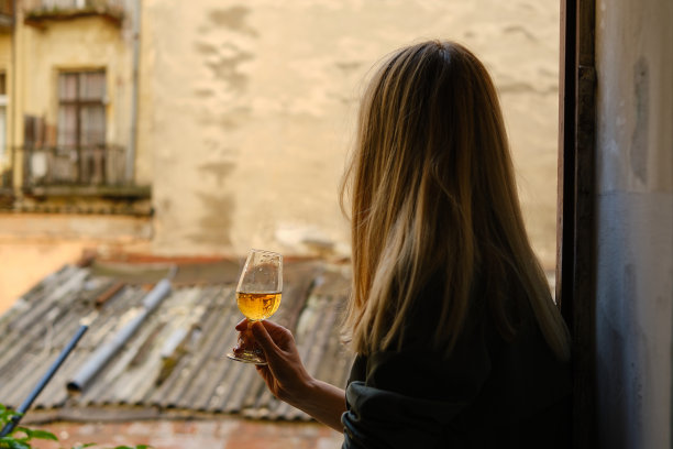 阳台上有个拿着酒杯的漂亮女孩。喝着白葡萄酒，享受这一刻。一个单独的庆祝节日。轻松的生活方式。快乐女人下班后休息。美丽的欧洲庭院图片下载