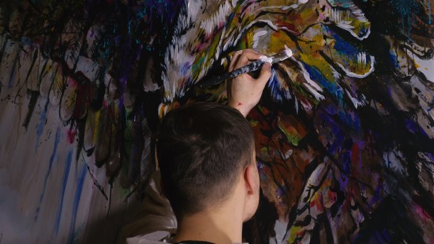 艺术家设计师在墙上画了一只鹰。工匠装饰用丙烯酸油彩作画。穿着油漆外套的画家。室内。图片下载