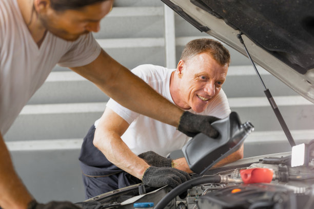 在加油站修理厂修理中心，修理工人正在往发动车上倒机油。概念工厂的设备维修和替换汽车业务行业。图片下载
