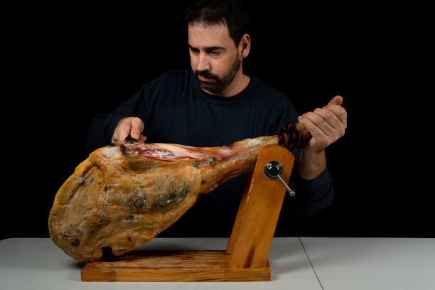 大胡子男子与火腿刀准备切一片典型的西班牙火腿孤立在黑色工作室背景。超级食物。美味的开胃菜图片下载