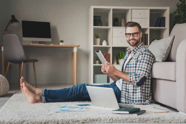 年轻帅哥的全身像侧面照片快乐正面微笑远程工作笔记本电脑坐在地板室内图片下载