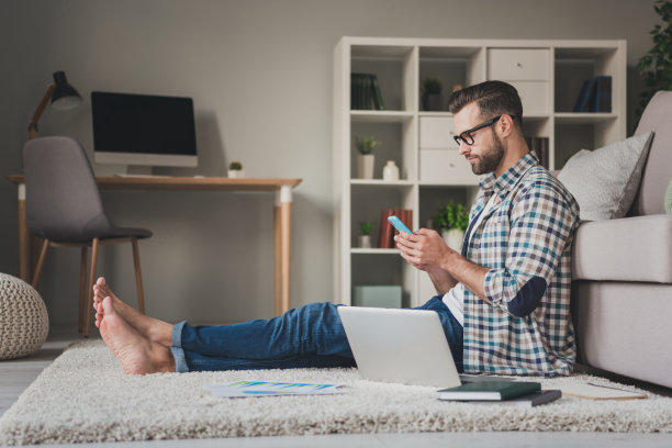 年轻帅哥的身段侧面照片看浏览手机远程工作笔记本电脑坐地板家图片下载