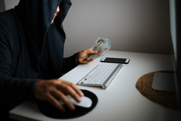 一名穿着连帽衬衫和面具的男子在黑暗中使用笔记本电脑黑客图片下载