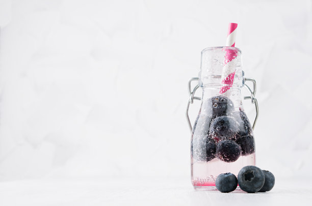冷鲜水果粉色成熟蓝莓饮料与苏打水，气泡，有趣的条纹吸管在简单柔和明亮的白色背景，复制空间。图片下载