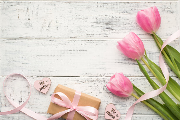 妇女节理念快乐。上面是一张用牛皮纸包裹的娇嫩郁金香和心形的小钉子放在空白的白色桌子上的近景照片图片下载